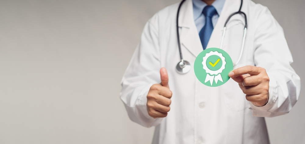 Doctor,Holding,A,Quality,Assurance,Symbol,While,Standing,In,The